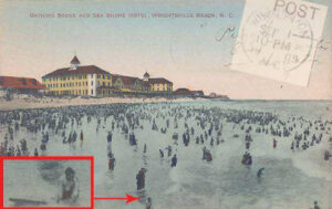 A vintage postcard of a beach scene with many people in the water and a large yellow building on the beach in the background. At the bottom of the postcard, a person is holding a surfboard-shaped object in the water.