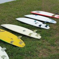 A variety of surfbards in a line on the grass.