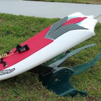 A red and white hydrofoil board on the grass.