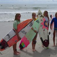 Four girls holding surfboards posing for a picture in front of the ocean