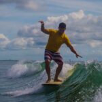 A man in yellow shirt and striped trunks riding a wave
