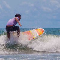 A man in a purple shirt and dark trunks surfing