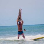 A man in striped trunks surfing while carrying a woman over his head